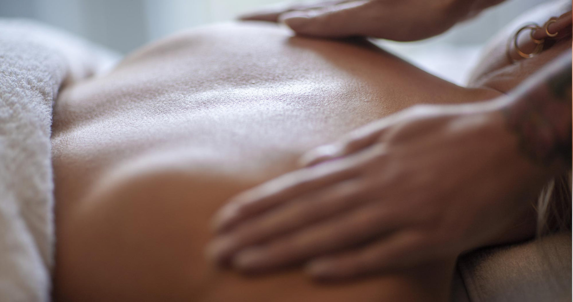 Kvinde ligger på maven og får massage på skulderbladene af to hænder